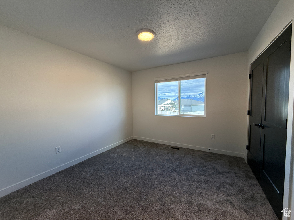 Unfurnished bedroom with dark colored carpet, visible vents, baseboards, and a textured ceiling