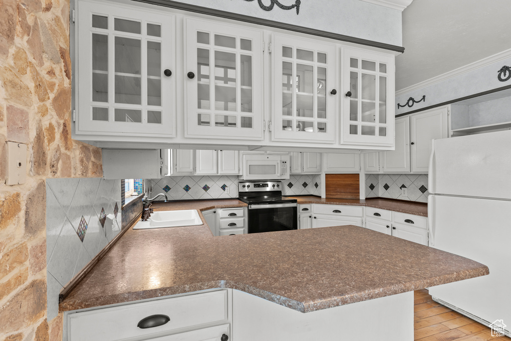 Kitchen with crown molding, a sink, white appliances, a peninsula, and decorative backsplash