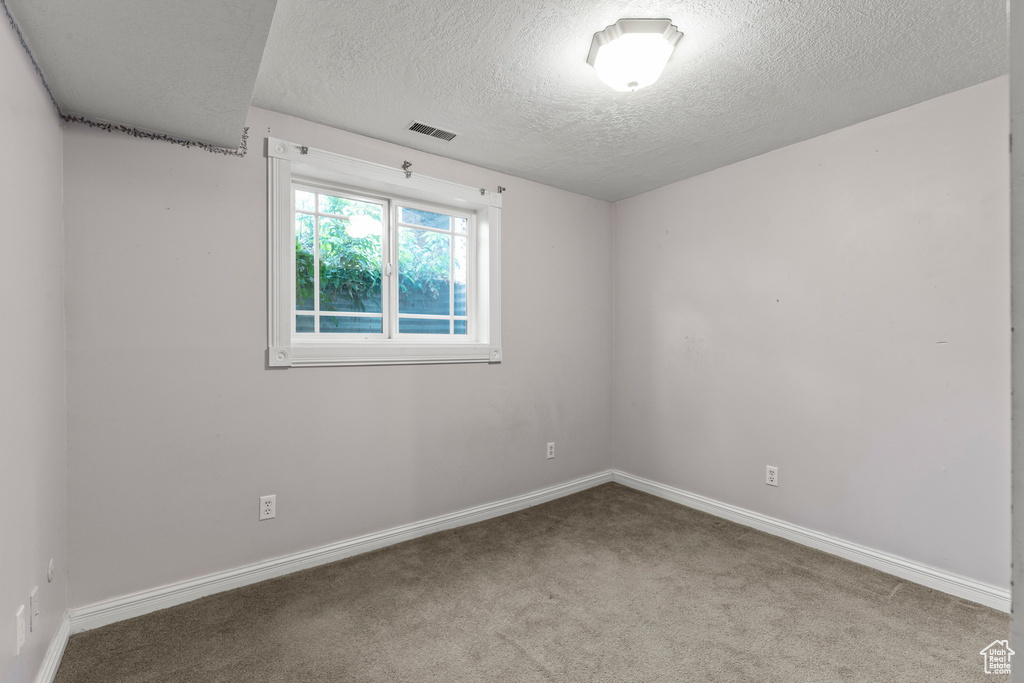 Carpeted spare room with a textured ceiling, visible vents, and baseboards