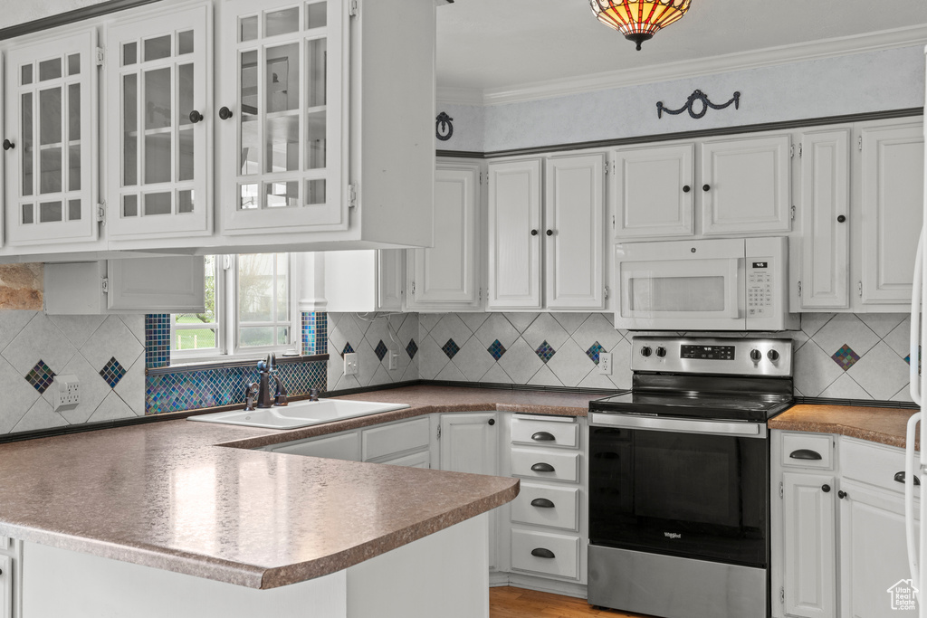 Kitchen with stainless steel electric range oven, white microwave, a peninsula, white cabinetry, and tasteful backsplash