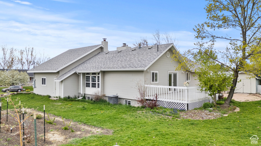 Back of property featuring a shingled roof, a storage shed, a wooden deck, a chimney, and a yard