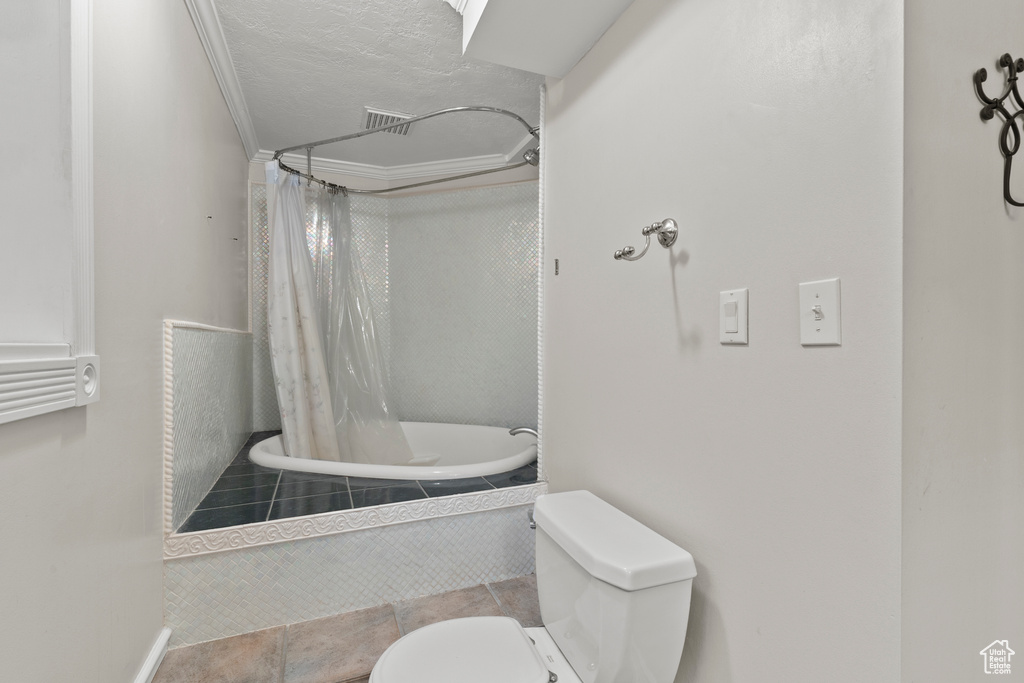 Bathroom featuring toilet, tiled shower / bath, tile patterned floors, and a textured ceiling