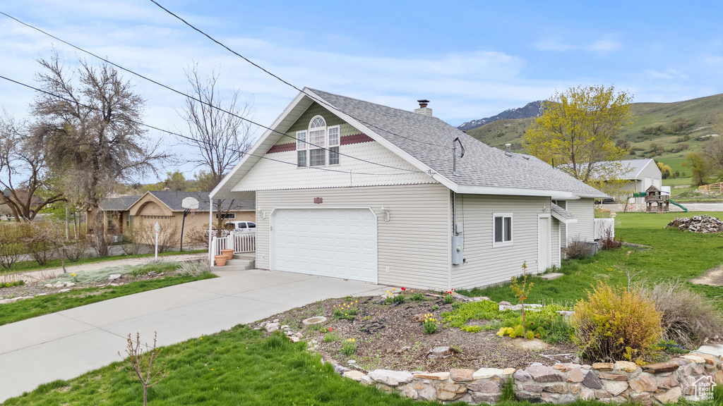 View of side of home with a shingled roof, a mountain view, a chimney, concrete driveway, and a yard
