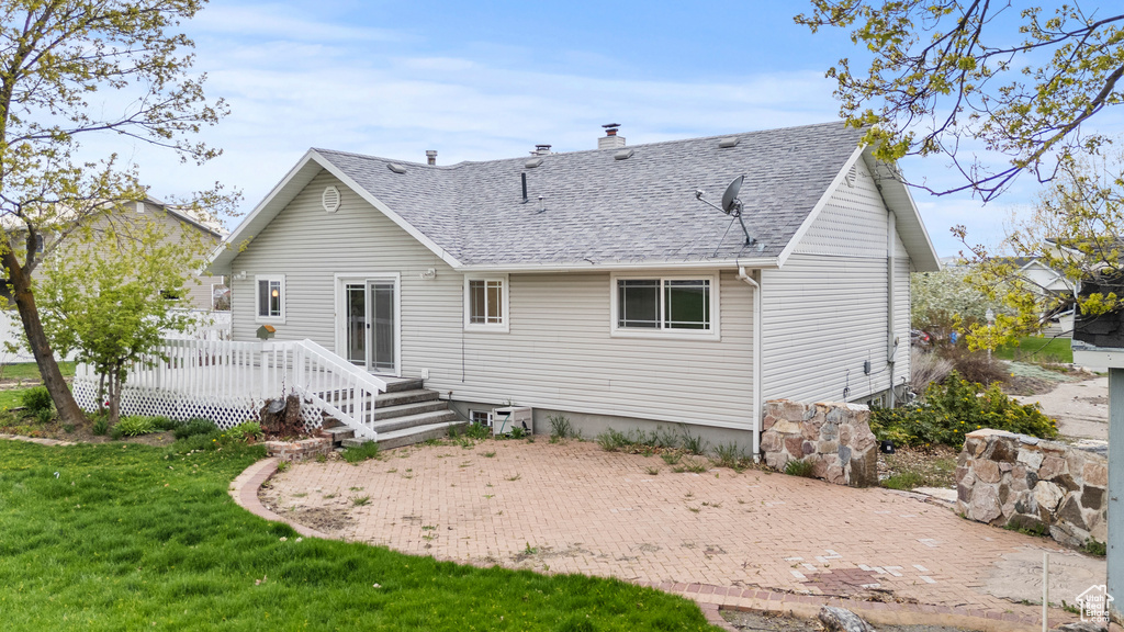 Back of house featuring roof with shingles, a wooden deck, a chimney, a patio area, and a yard