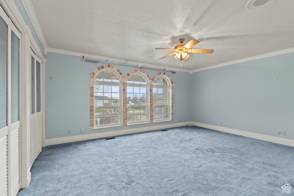 Unfurnished room with ceiling fan, visible vents, crown molding, baseboards, and carpet