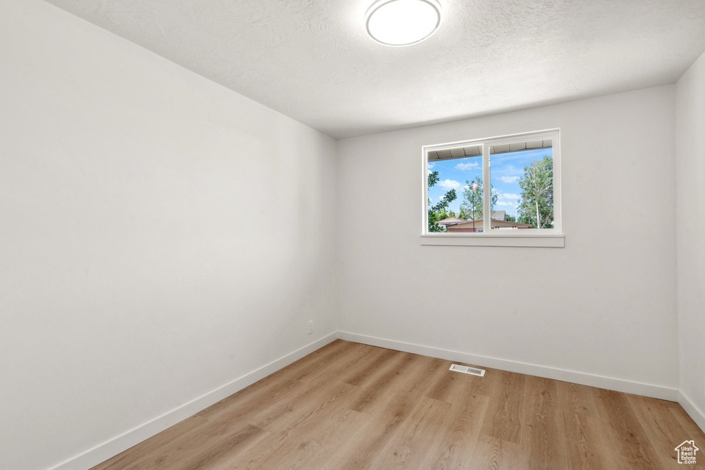Empty room with baseboards, light wood finished floors, and a textured ceiling