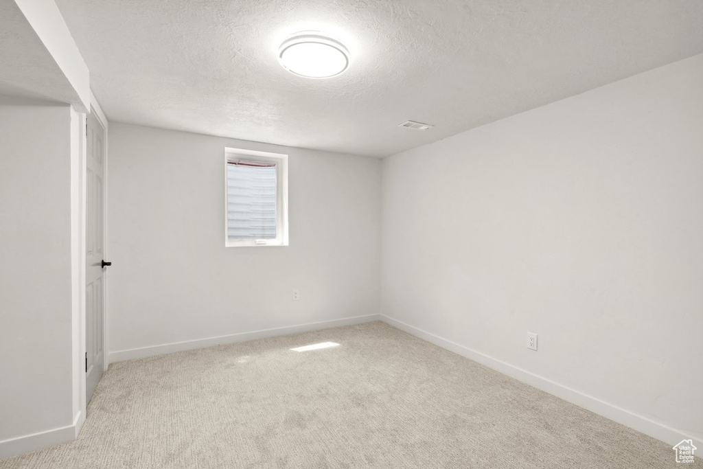 Spare room with a textured ceiling, baseboards, and light colored carpet