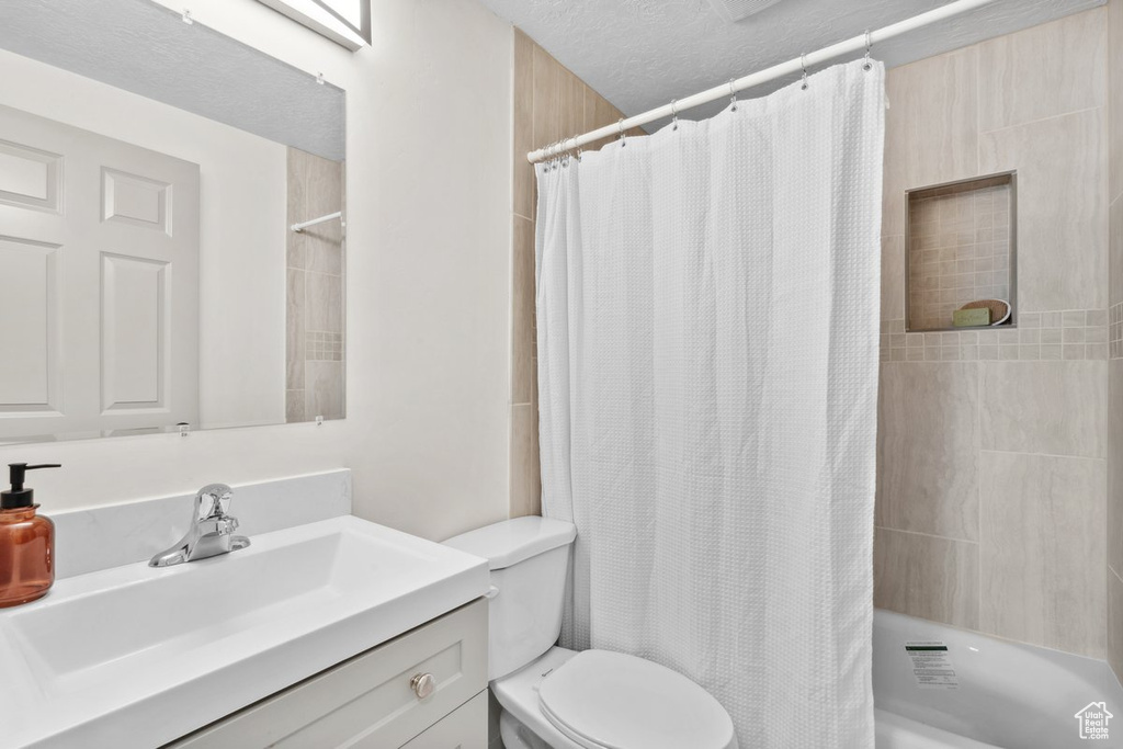 Bathroom with vanity, toilet, shower / tub combo with curtain, and a textured ceiling