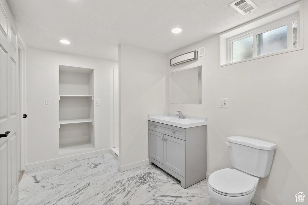 Bathroom with baseboards, vanity, toilet, marble look tiles, and recessed lighting