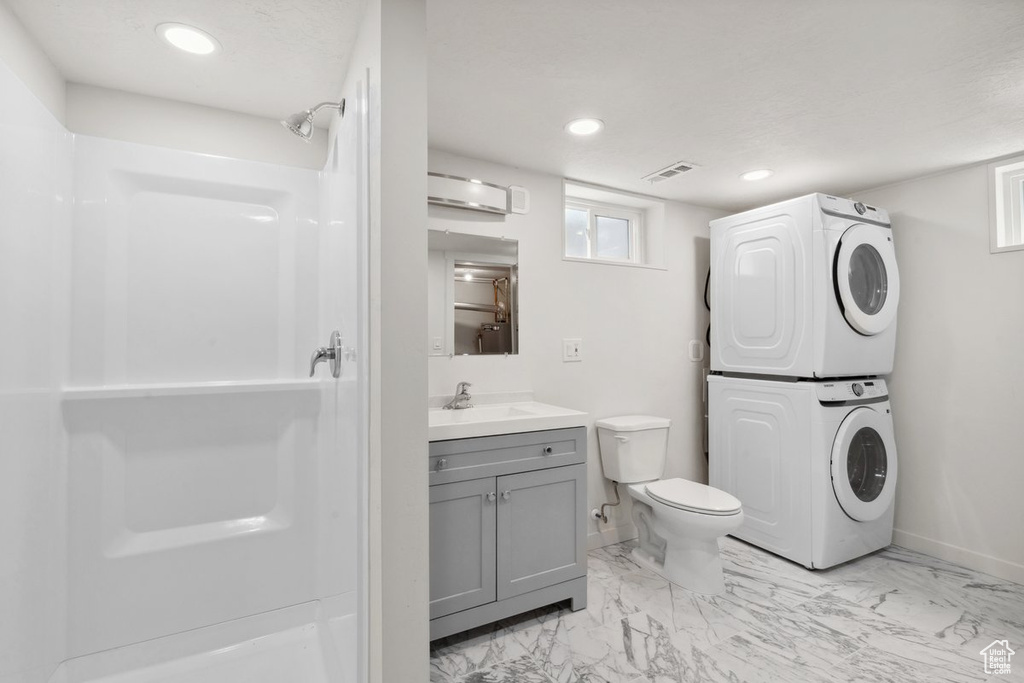 Bathroom with stacked washer and clothes dryer, a shower, vanity, baseboards, and recessed lighting