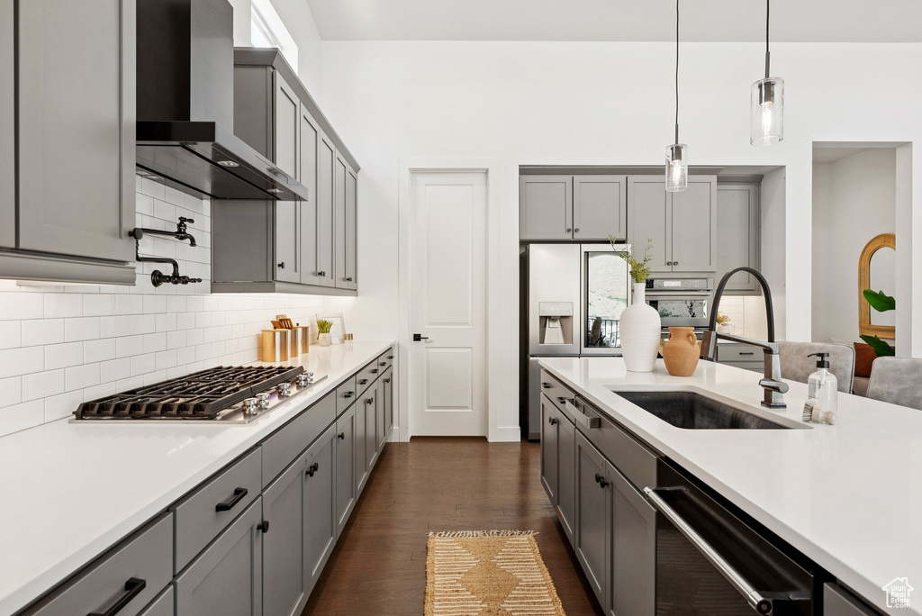 Kitchen with wall chimney exhaust hood, appliances with stainless steel finishes, a sink, and gray cabinetry