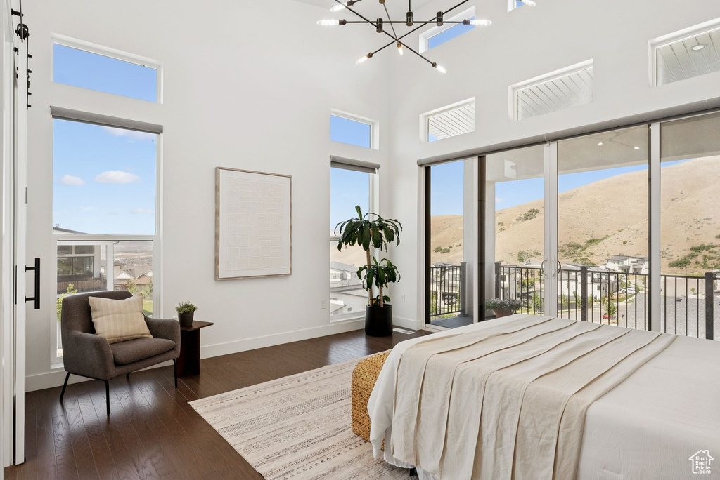 Bedroom with access to exterior, a chandelier, wood finished floors, baseboards, and a towering ceiling