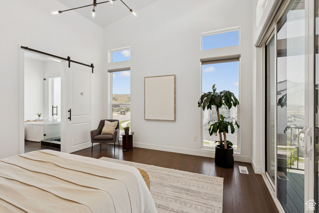 Bedroom with a barn door, a towering ceiling, dark wood-type flooring, baseboards, and ensuite bathroom