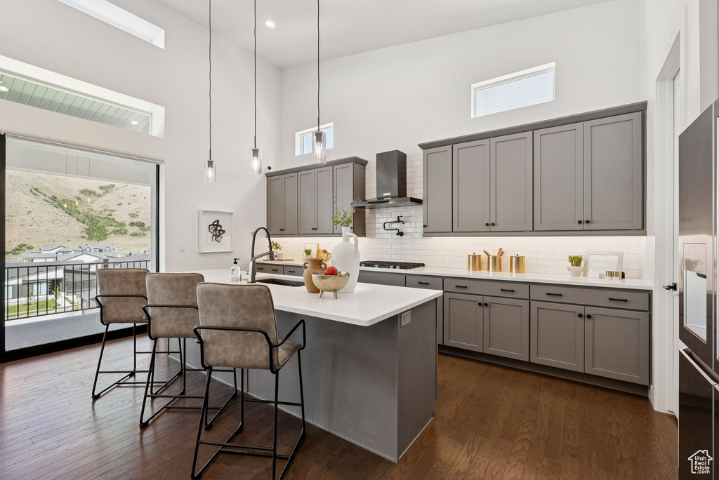 Kitchen featuring gray cabinetry, wall chimney exhaust hood, a high ceiling, a sink, and gas stovetop