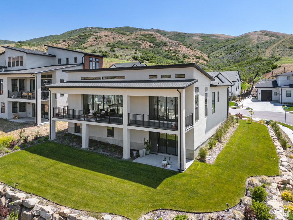 Rear view of property with stucco siding, a balcony, a mountain view, and a yard