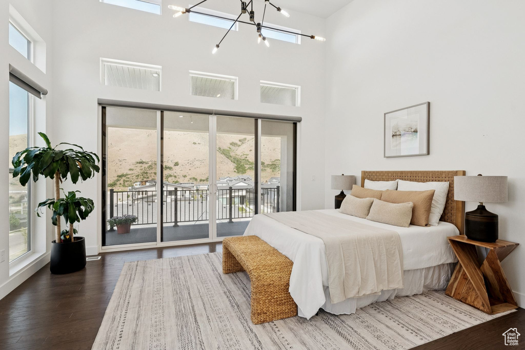 Bedroom featuring access to outside, a towering ceiling, wood finished floors, a chandelier, and baseboards
