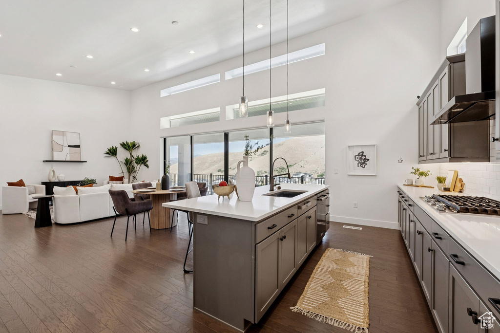 Kitchen featuring a sink, gray cabinetry, stainless steel appliances, wall chimney exhaust hood, and a high ceiling