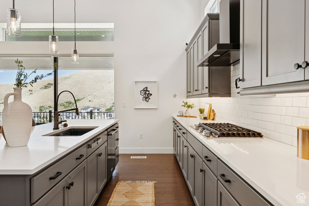 Kitchen featuring wall chimney range hood, a sink, gray cabinets, baseboards, and tasteful backsplash