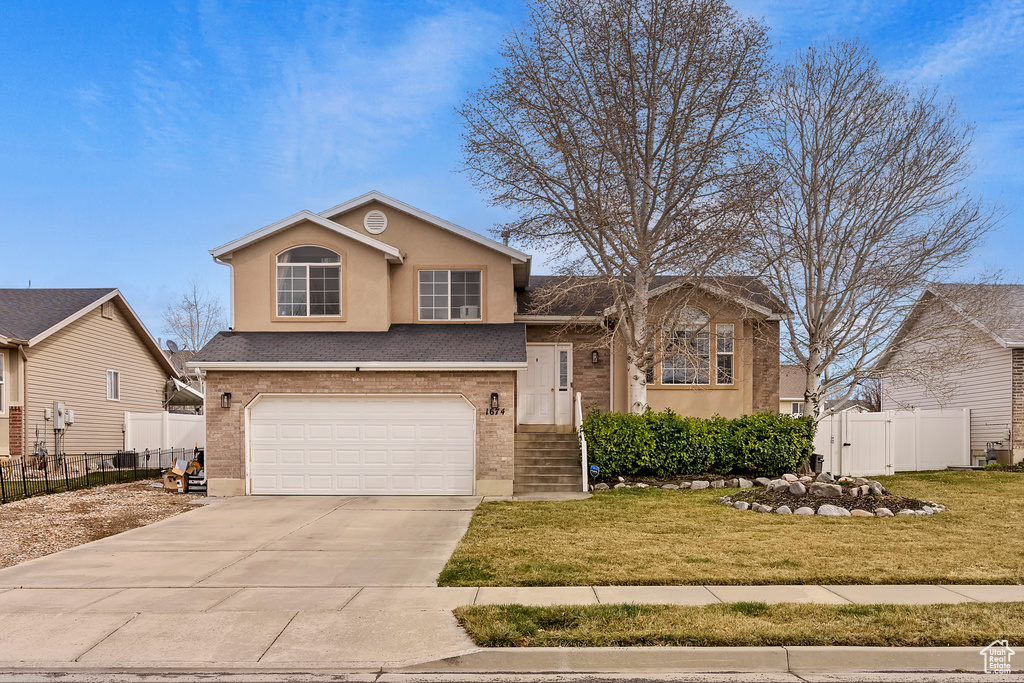 Split level home featuring driveway, a gate, fence, a front lawn, and a garage