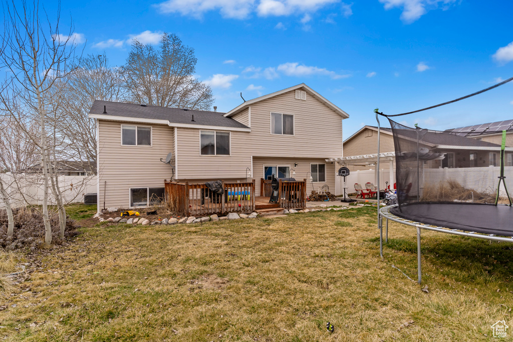 Rear view of house featuring a trampoline, fence, a yard, and a deck