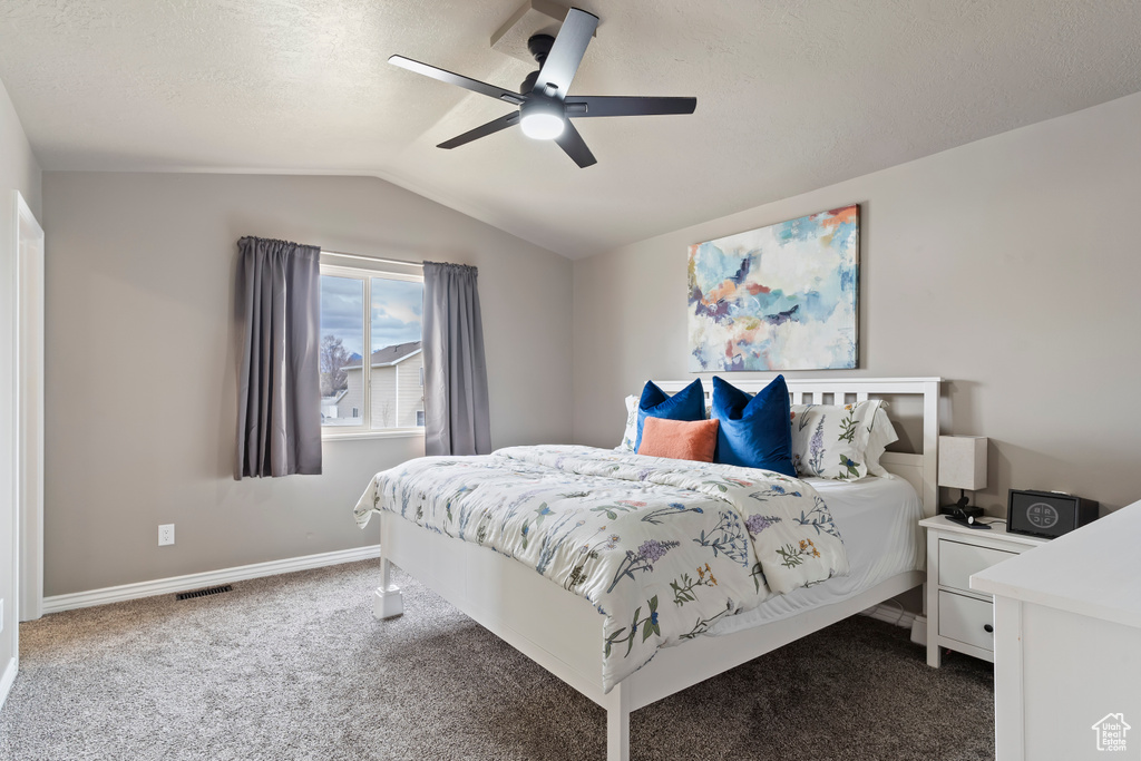 Bedroom featuring dark colored carpet, vaulted ceiling, baseboards, visible vents, and a ceiling fan