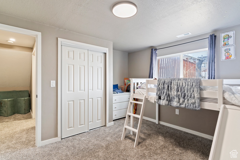 Carpeted bedroom featuring baseboards, visible vents, a closet, and a textured ceiling