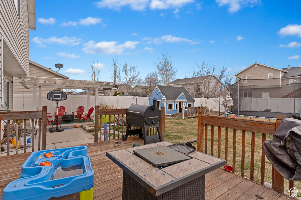 Wooden terrace with a fenced backyard, grilling area, an outdoor fire pit, a pergola, and a lawn