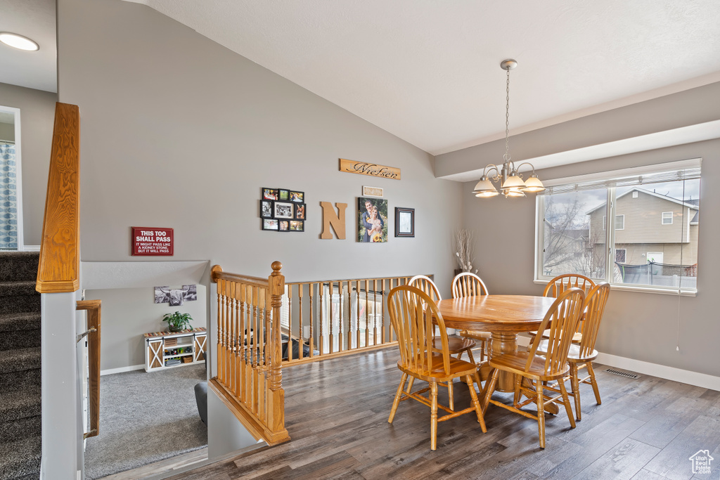 Dining area with baseboards, a notable chandelier, wood finished floors, and vaulted ceiling