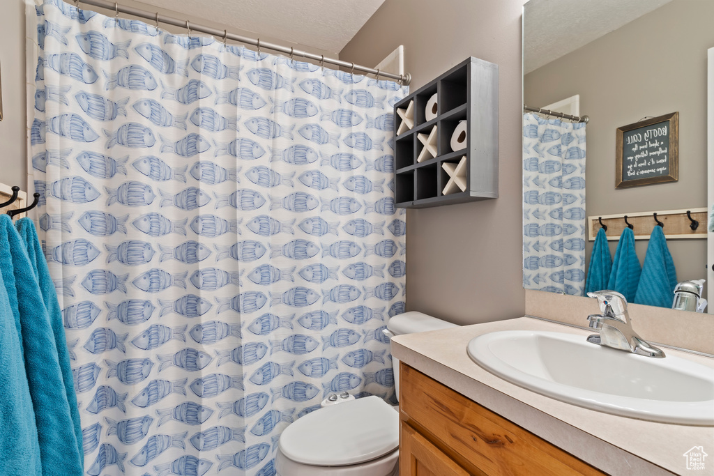 Bathroom featuring curtained shower, toilet, and vanity