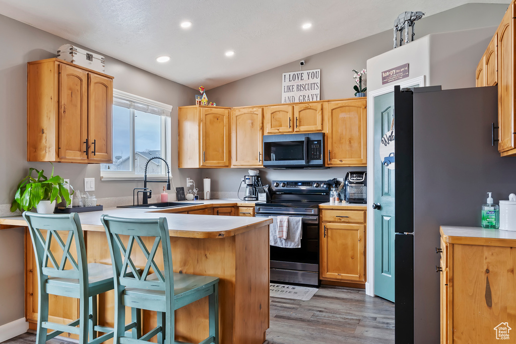 Kitchen with light countertops, lofted ceiling, a sink, a peninsula, and appliances with stainless steel finishes