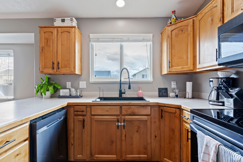 Kitchen with black microwave, dishwashing machine, light countertops, and a sink