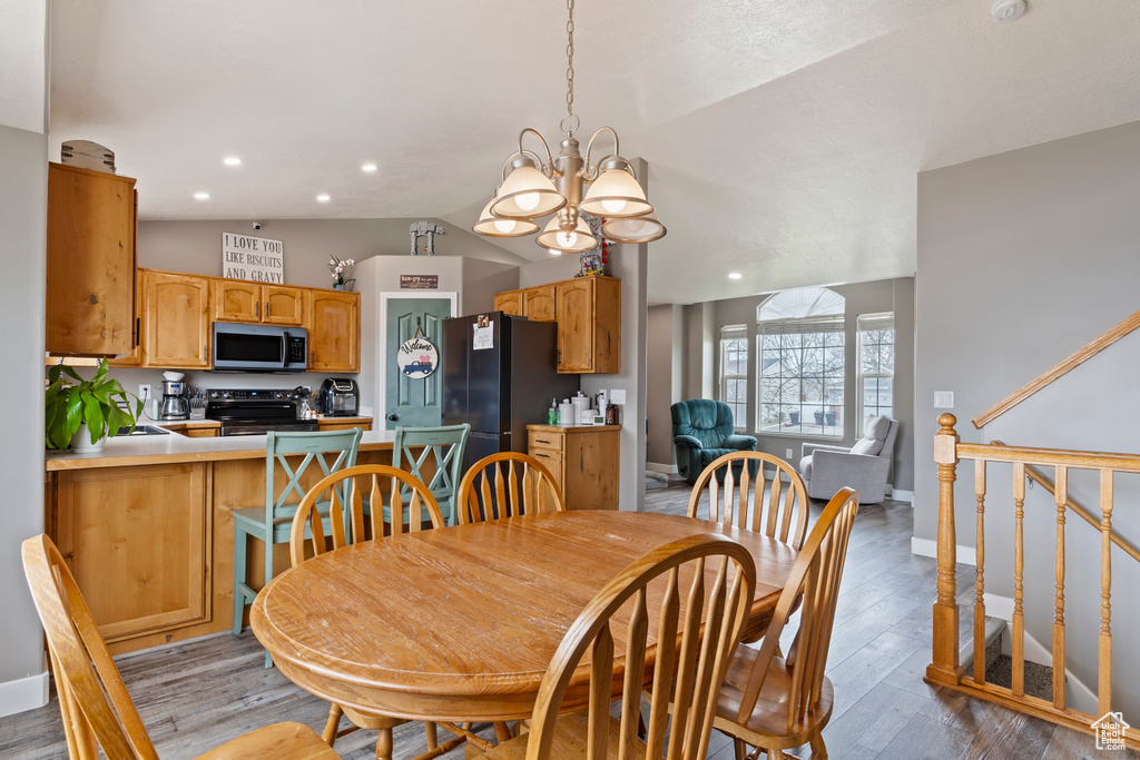 Dining space featuring a notable chandelier, vaulted ceiling, light wood finished floors, baseboards, and recessed lighting