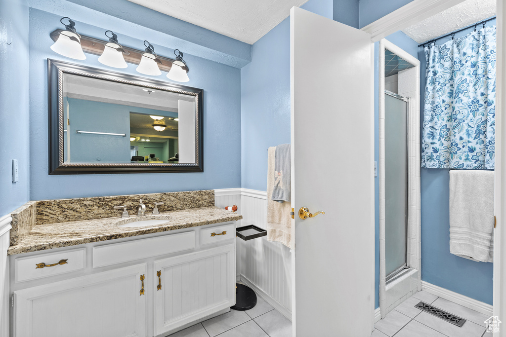 Bathroom with an enclosed shower, tile patterned flooring, vanity, and wainscoting
