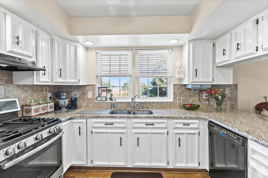 Kitchen featuring stainless steel gas stove, black dishwasher, under cabinet range hood, and white cabinetry