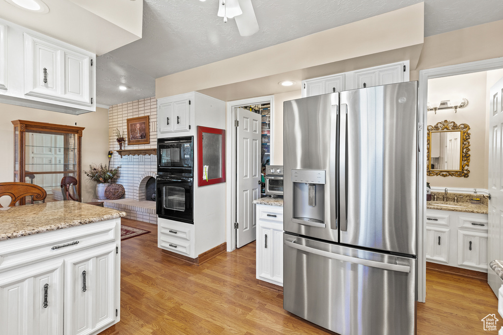 Kitchen featuring stainless steel fridge with ice dispenser, white cabinetry, light stone countertops, ceiling fan, and light wood-type flooring