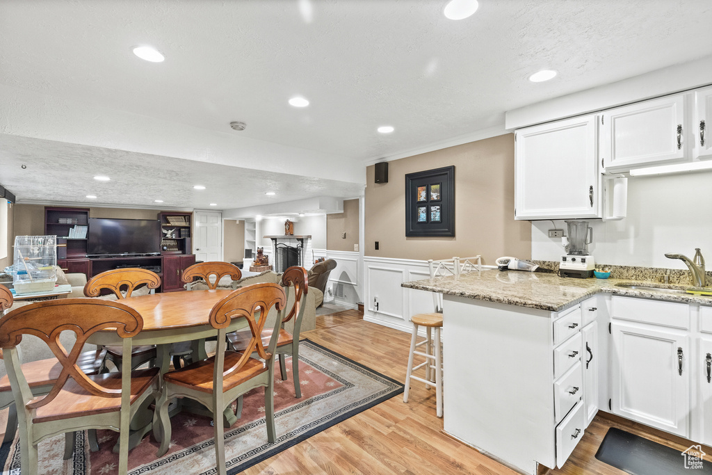 Dining area with light wood finished floors, a wainscoted wall, and recessed lighting