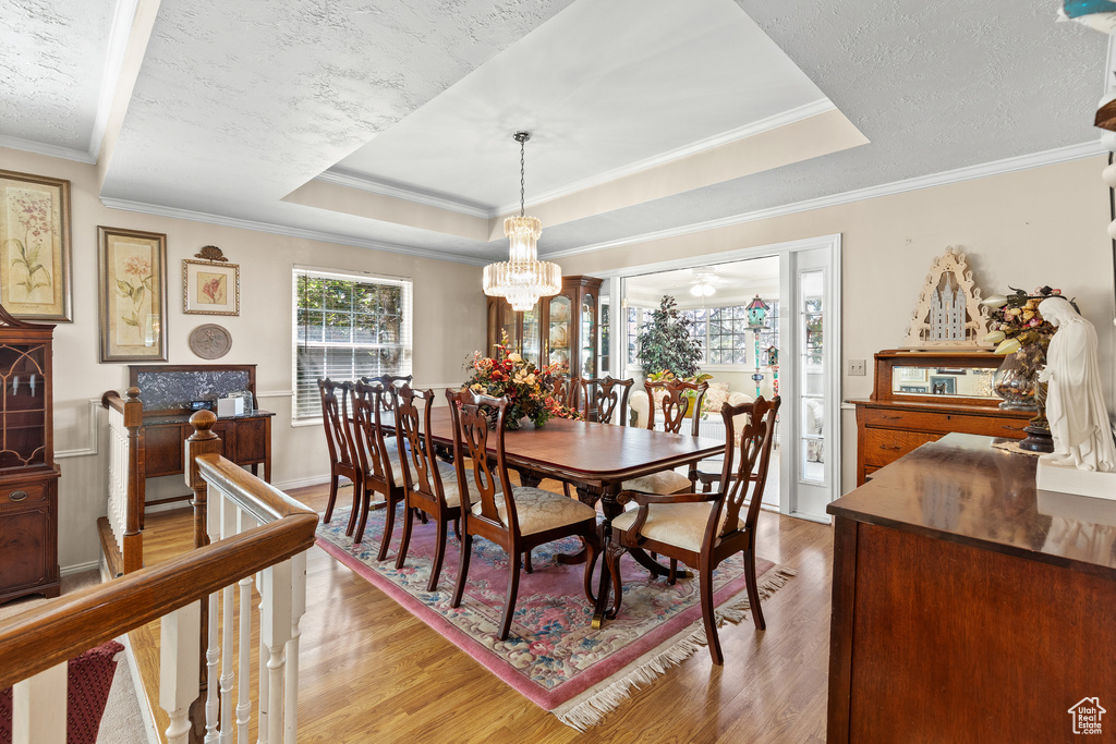Dining space with light wood-type flooring, a chandelier, a raised ceiling, and crown molding
