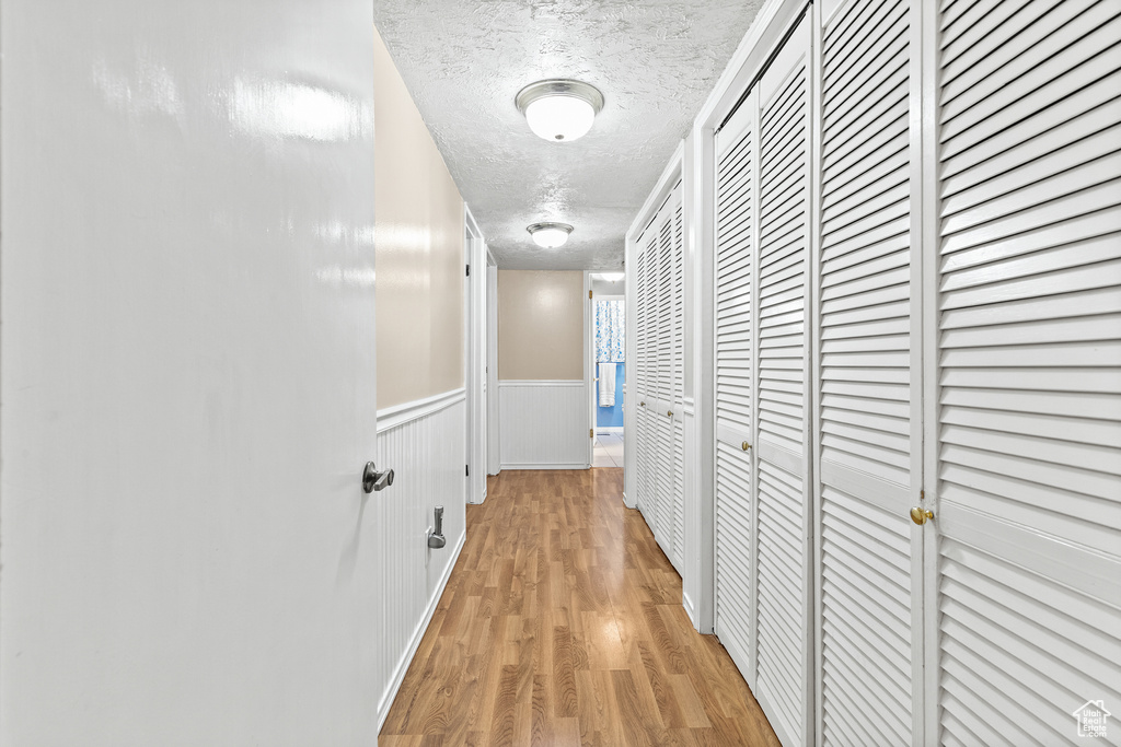 Hall featuring a textured ceiling, light wood finished floors, and a wainscoted wall