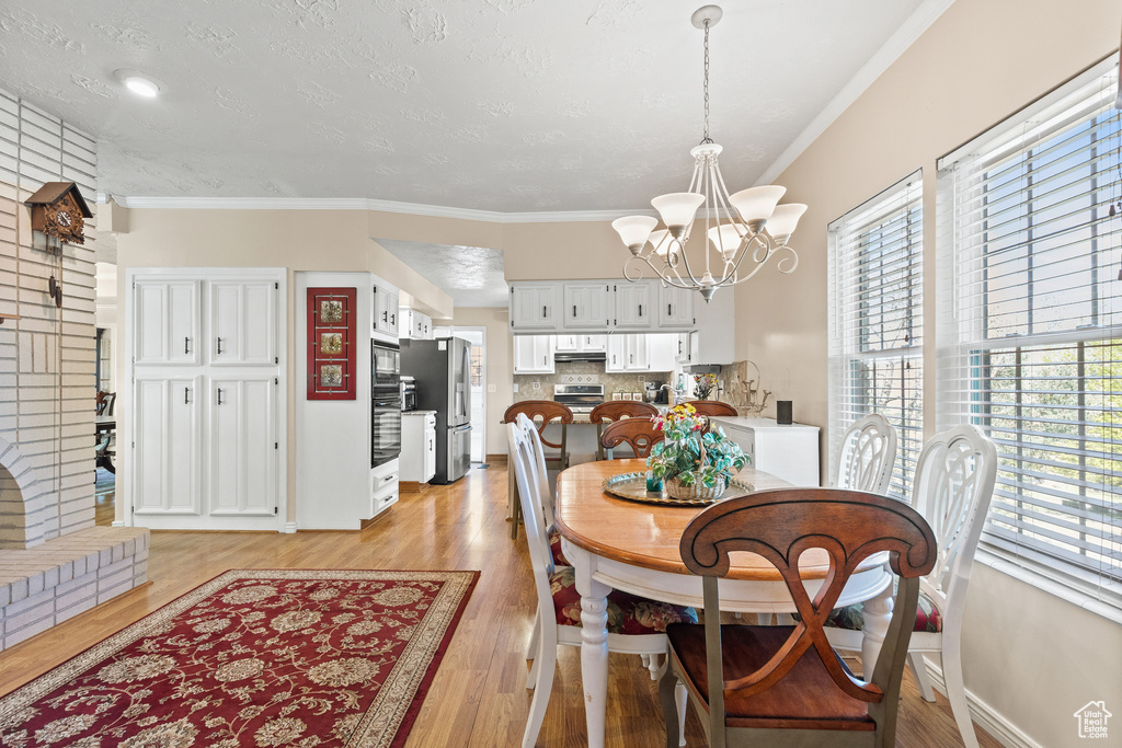 Dining room with healthy amount of natural light, a chandelier, light wood finished floors, and crown molding