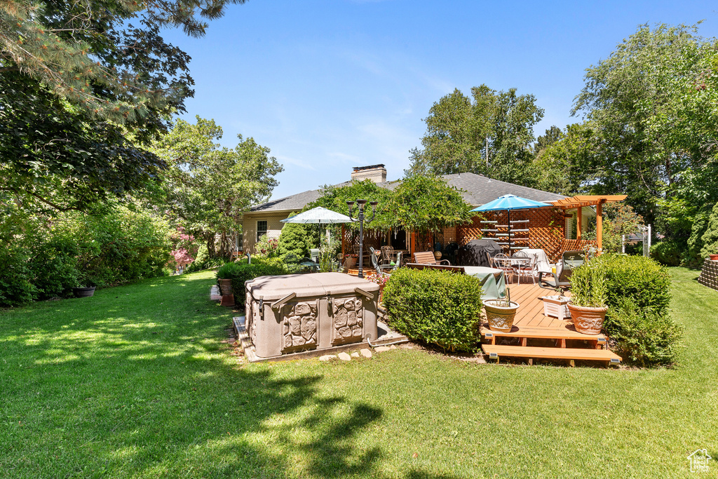 View of green lawn with a wooden deck and a hot tub