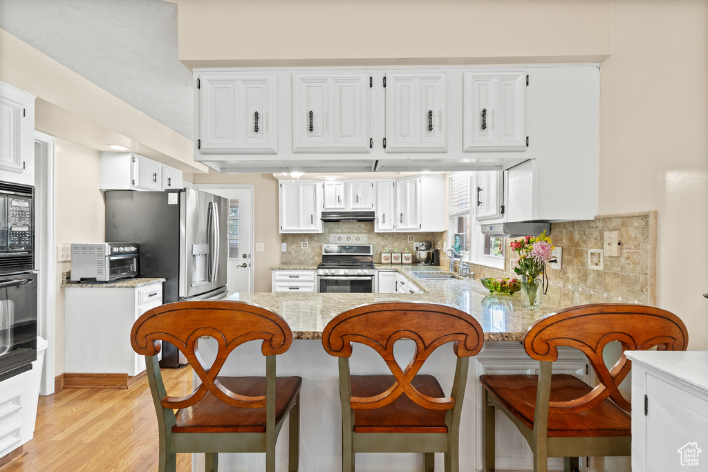 Kitchen featuring black appliances, under cabinet range hood, a peninsula, tasteful backsplash, and light wood-style flooring
