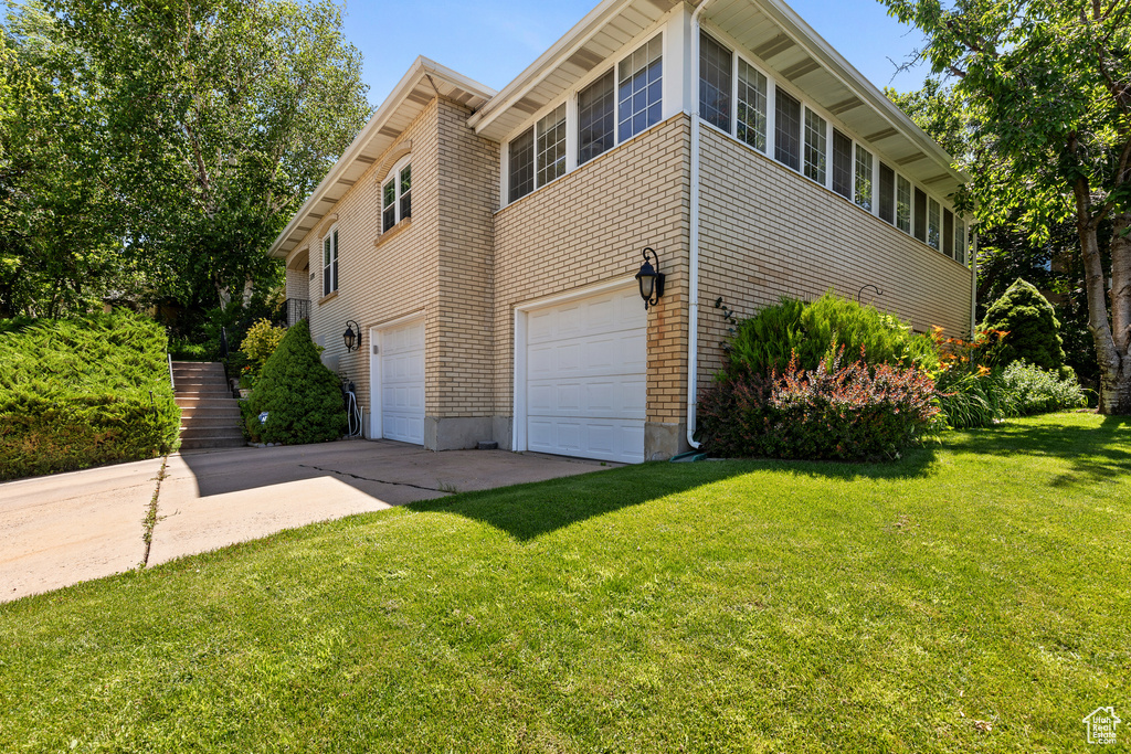 View of side of property with an attached garage, driveway, and a yard