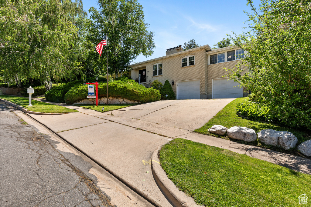 View of front of property featuring concrete driveway, a garage, brick siding, and a chimney