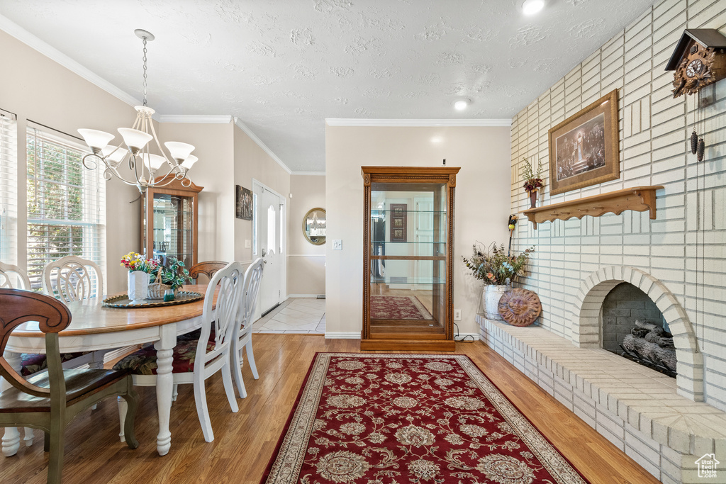 Dining space with a chandelier, light wood-type flooring, a textured ceiling, a brick fireplace, and crown molding
