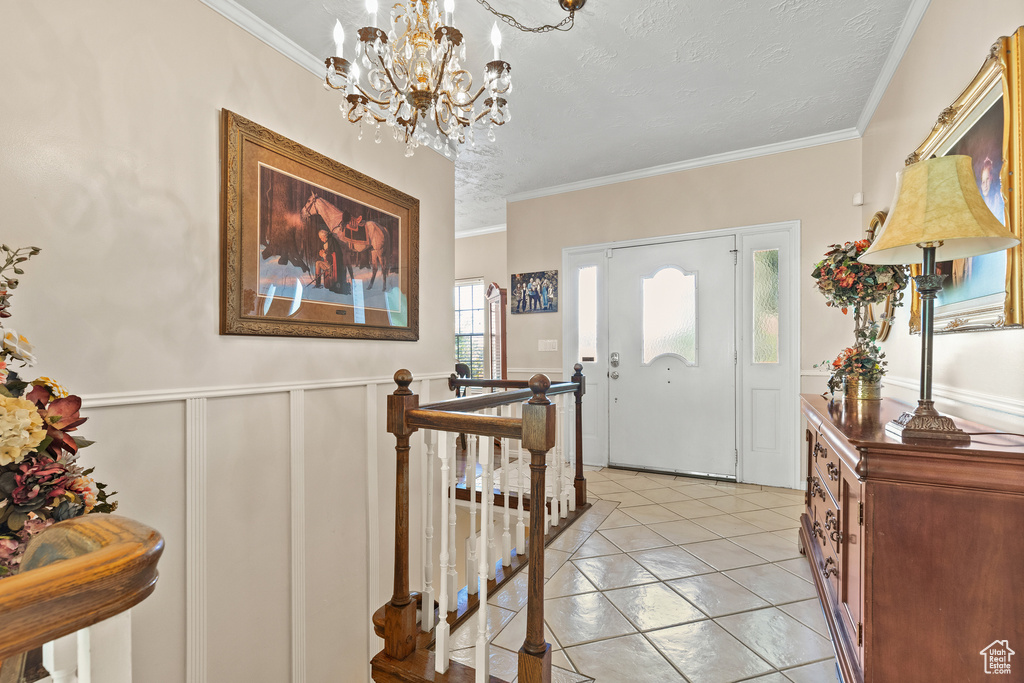 Foyer entrance with a chandelier, crown molding, wainscoting, a textured ceiling, and light tile patterned floors