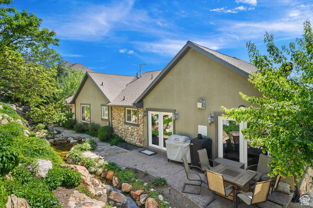 Back of house featuring a patio, stone siding, stucco siding, french doors, and a shingled roof