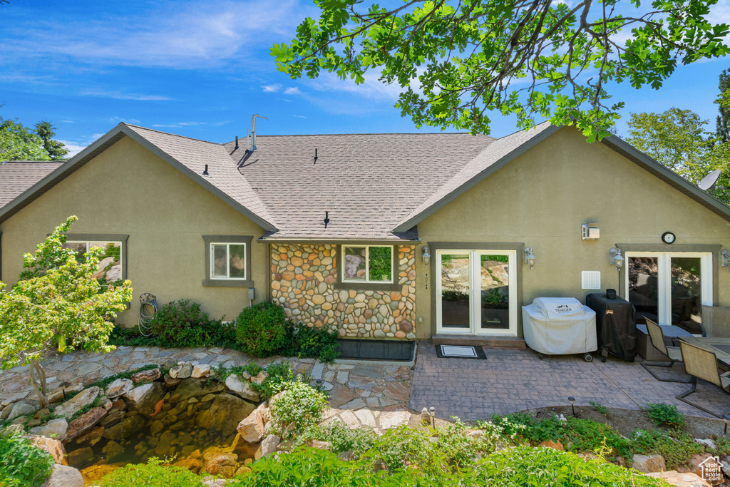 Back of house featuring a shingled roof, stucco siding, a patio, and stone siding
