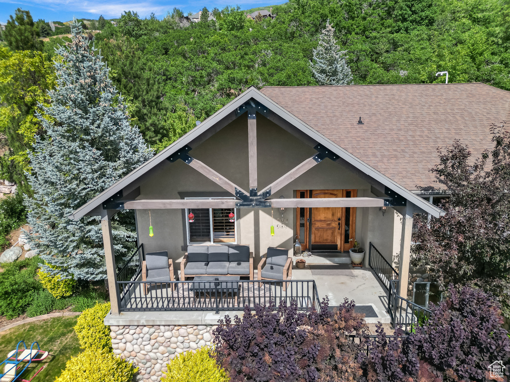 View of front of house with an outdoor living space, stucco siding, a patio area, roof with shingles, and a wooded view