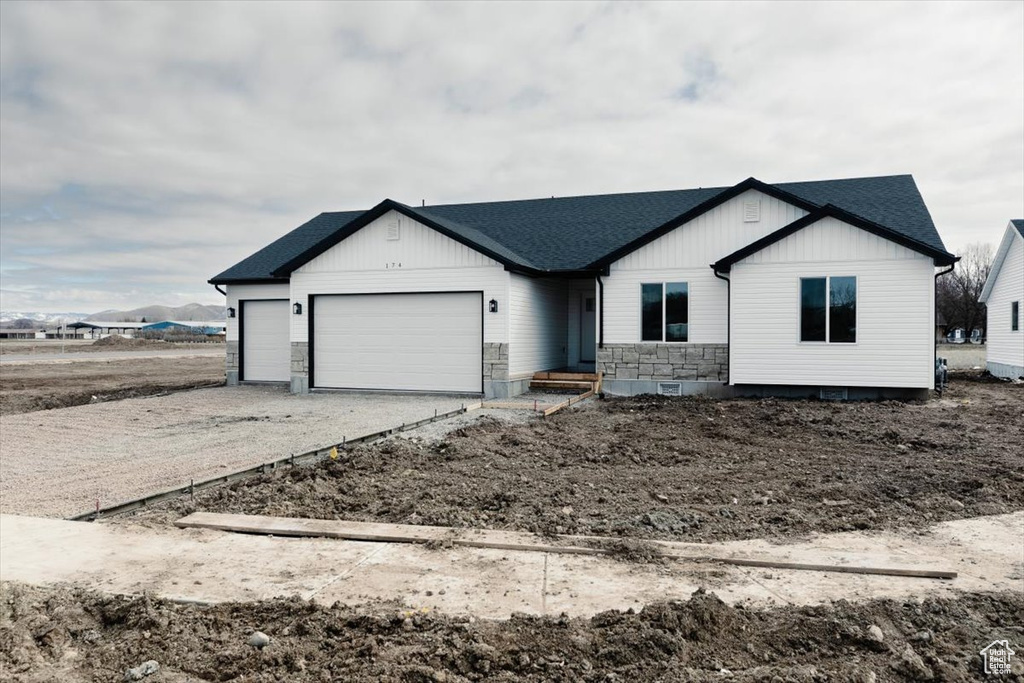 View of front facade with stone siding, an attached garage, board and batten siding, driveway, and a shingled roof