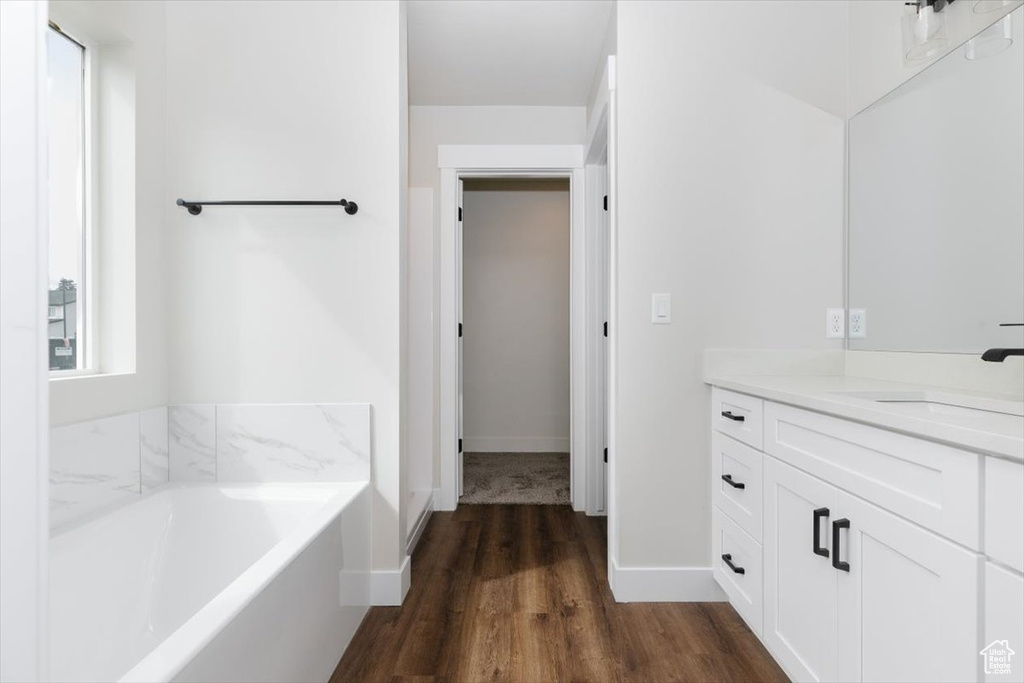 Bathroom featuring a bath, baseboards, wood finished floors, and vanity